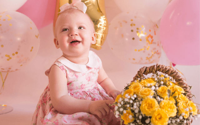 A smiling little girl  wearing a stylish pink Christening Gown 
